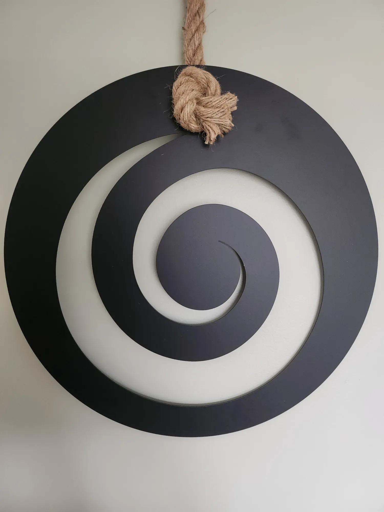A large black koru spiral, cut from a single disc, hanging on the wall of the Havening room from a knotted rope.