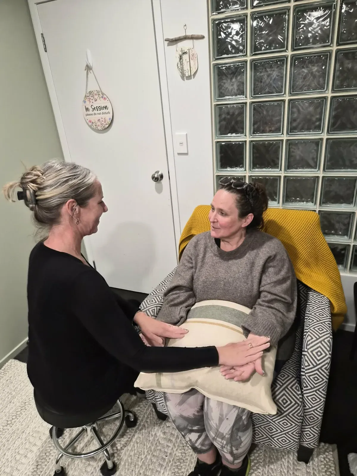 Lisa resting her hands lightly across a client's open palms, the two of them talking face to face in the session room.