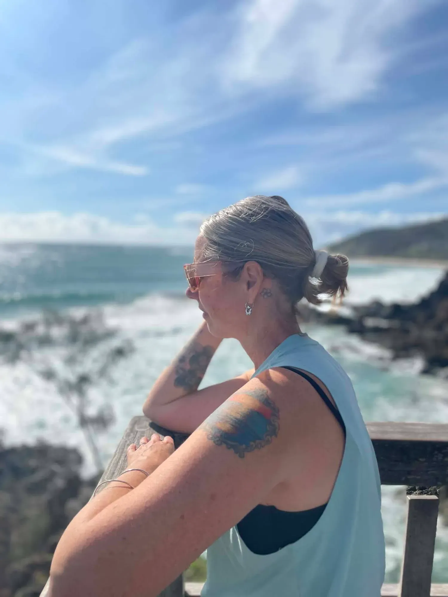 Lisa leaning on a wooden rail above the rocks, looking out over the sea on a bright day.