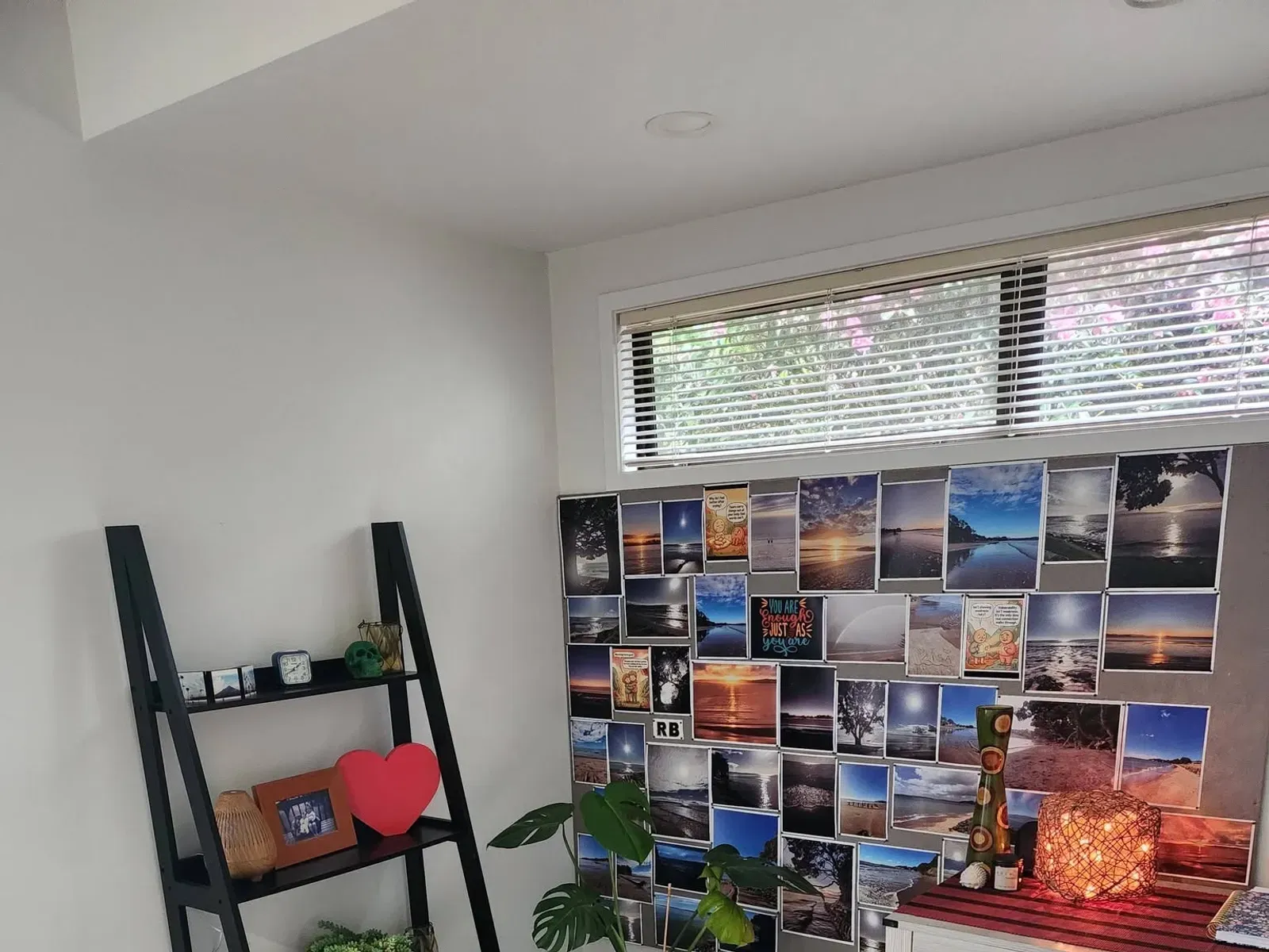 Another corner of the session room: a desk with a woven lamp, a monstera in a white pot, and a pinboard covered in photographs of Red Beach.