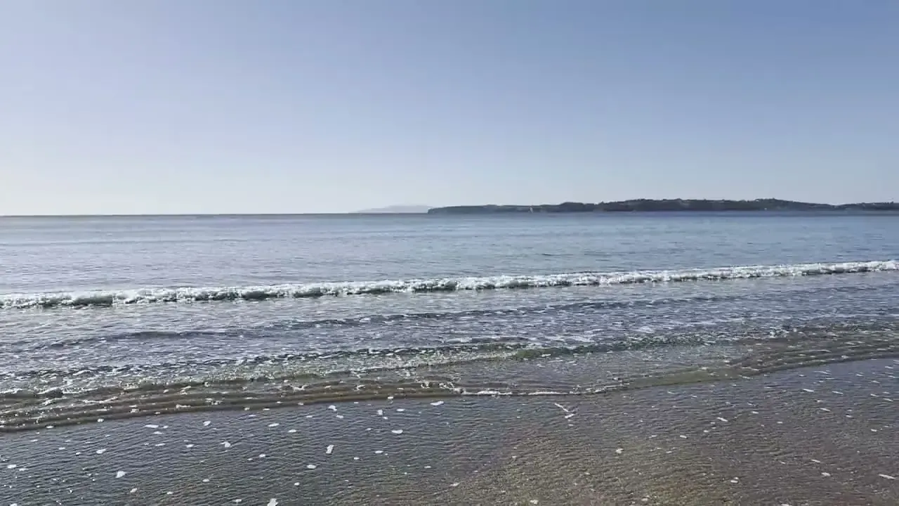 The sea at Red Beach on a clear morning, small waves rolling onto the sand.